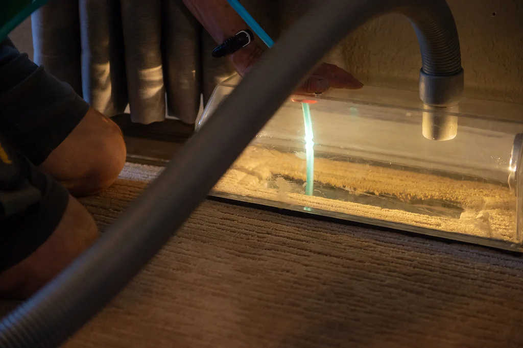 Technician using clear vacuum seal and blue air hose to remove debris from dusty vent raising question will cleaning air ducts help with dust at home.
